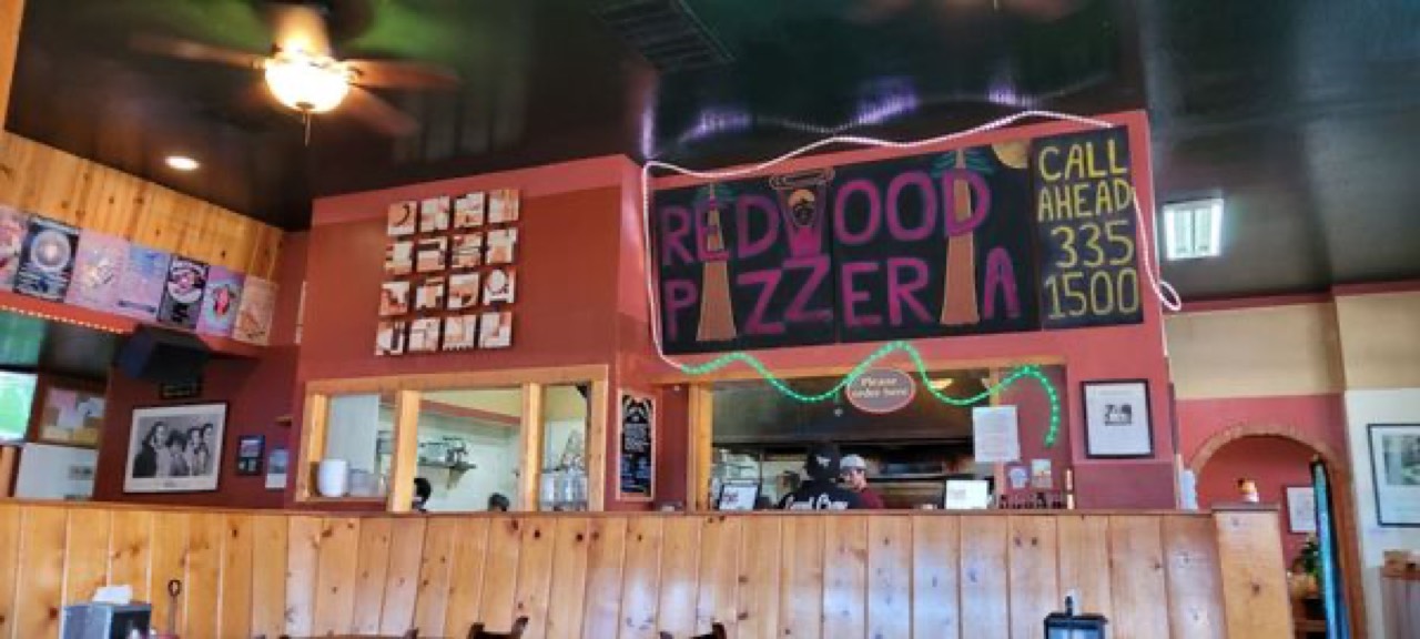 Dining room interior with Redwood Pizzeria chalkboard sign and call-ahead number displayed.