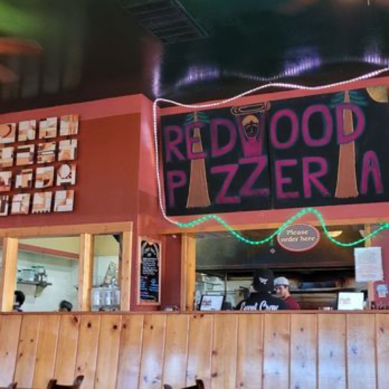 Order counter with neon-lit Redwood Pizzeria chalkboard sign above kitchen window.
