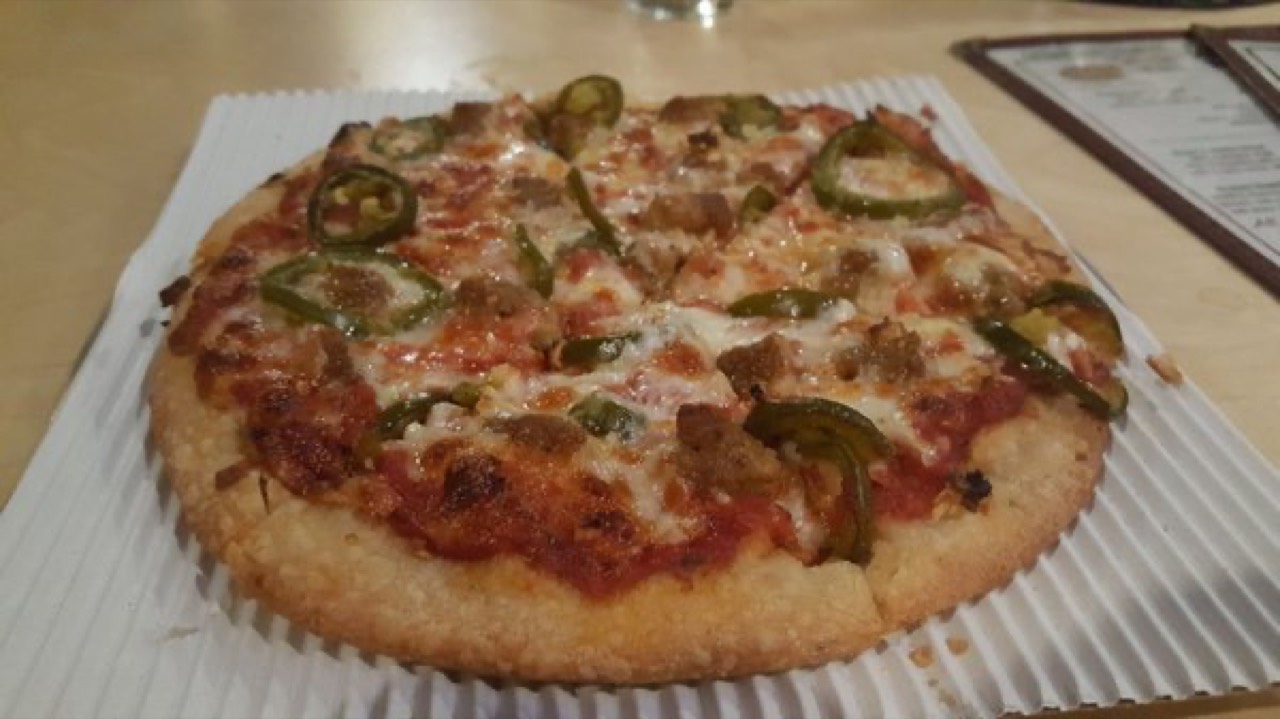 Small pizza topped with jalapeños, sausage, and melted mozzarella on corrugated board.