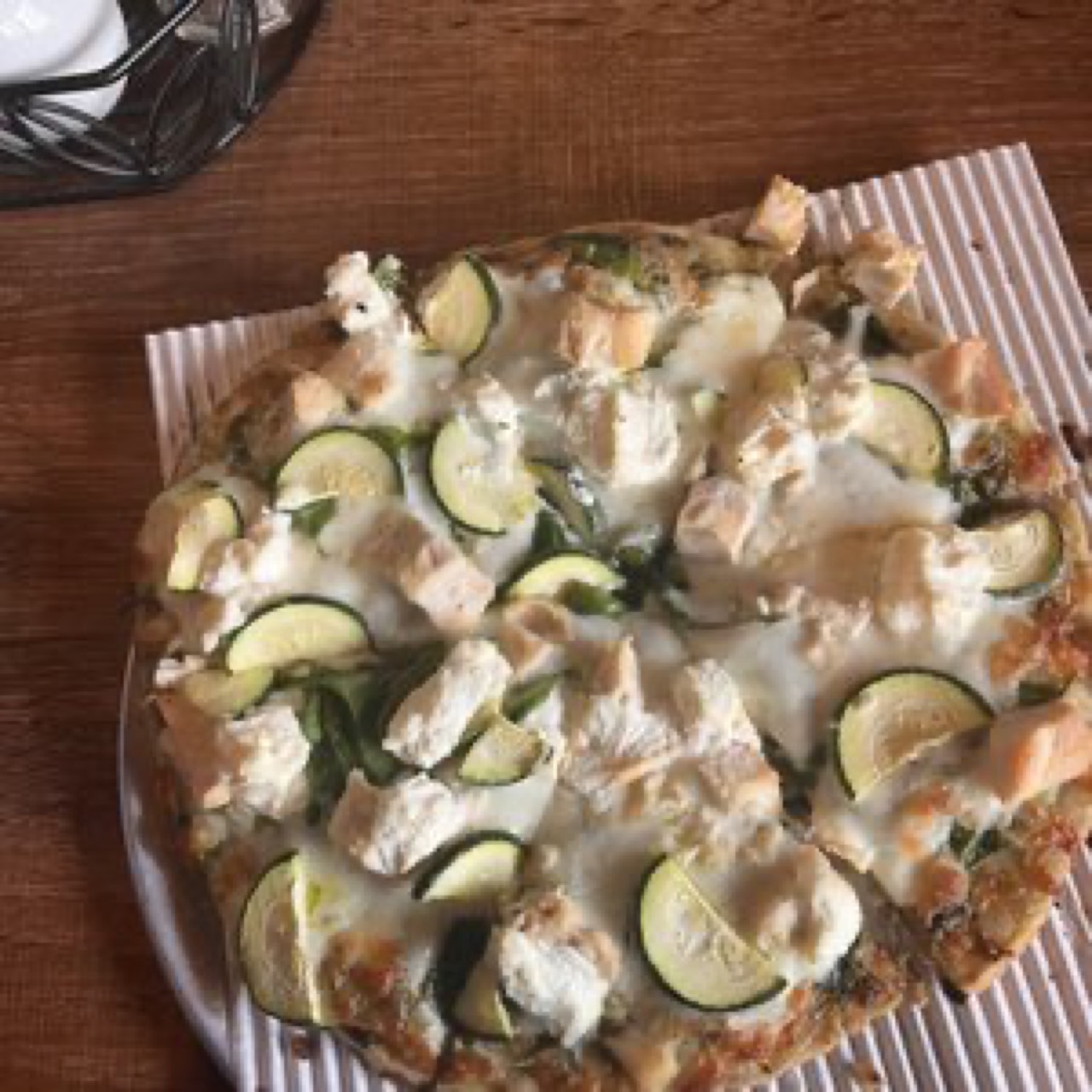 White pizza with zucchini, chicken, and ricotta on a round pan, top-down.