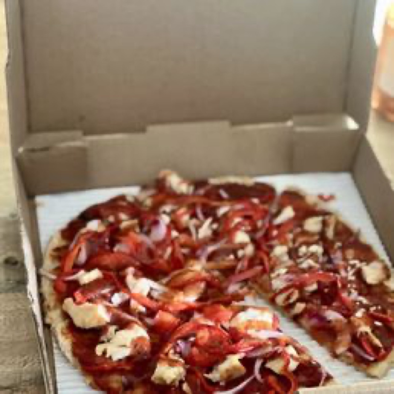 Takeout box open showing red-sauced pizza with roasted chicken and red onions.